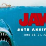 Jaws 50th Anniversary poster featuring the iconic great white shark rising from the ocean beneath an unsuspecting swimmer.